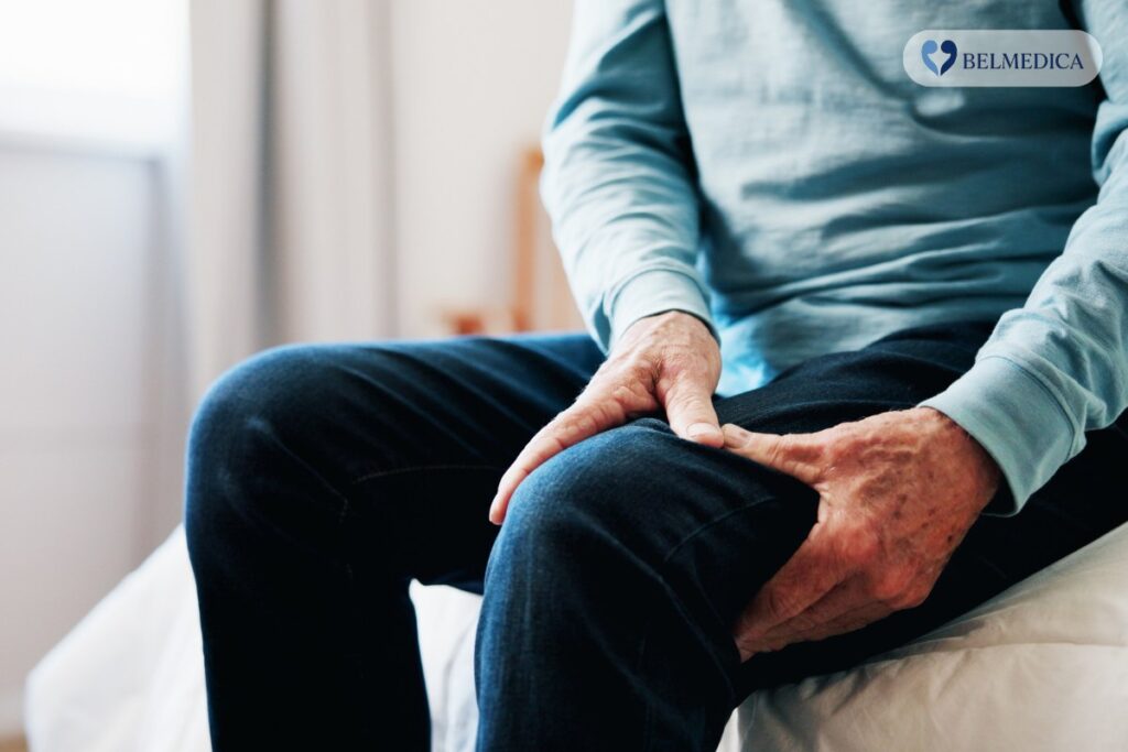 Starszy mężczyzna na brzegu łóżka trzyma się za kolano. reumatolog Łomża prywatnie